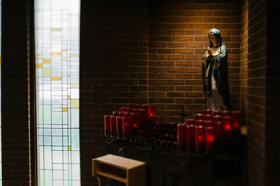 Imagem de Nossa Senhora acima de velas votivas vermelhas
